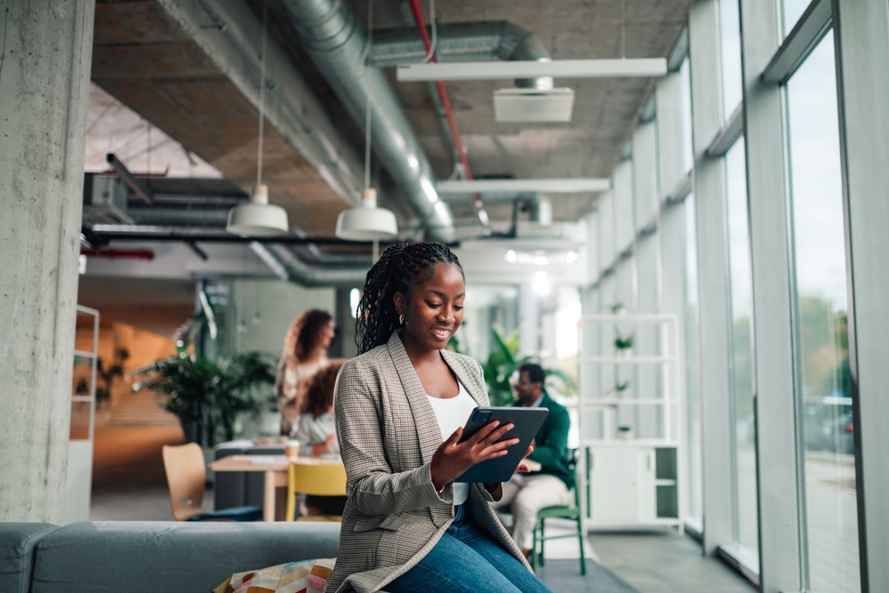 Young,Black,Businesswoman,Sitting,,Smiling,,And,Using,A,Digital,Tablet